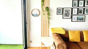Ein modernes Wohnzimmer mit einem braunen Sofa, einem kleinen weißen Sessel, einem Holz-Pflanzentisch und gerahmten Bildern an der Wand.