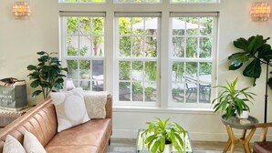 A spacious living room with a high ceiling, large windows, a leather sofa, a glass coffee table, and a potted plant. - Spa Like Stay at the Award Winning Britt Bungalow in the Heart of Jacksonville (Jacksonville)