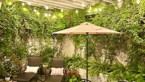 A covered patio area with a stone-tiled floor, outdoor furniture, string lights, and lush greenery. - Spa Like Stay at the Award Winning Britt Bungalow in the Heart of Jacksonville (Jacksonville)