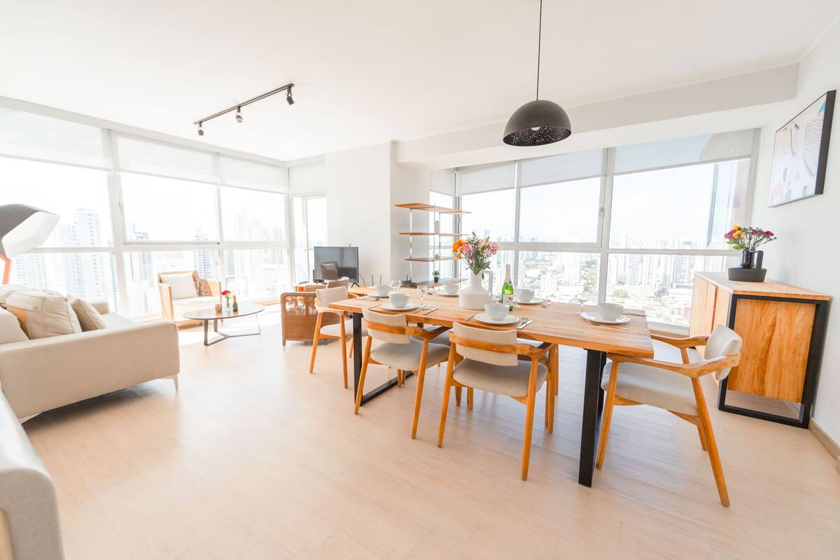 Ein modernes Wohnzimmer mit Essbereich, großen Fenstern und Blick auf die Stadt.