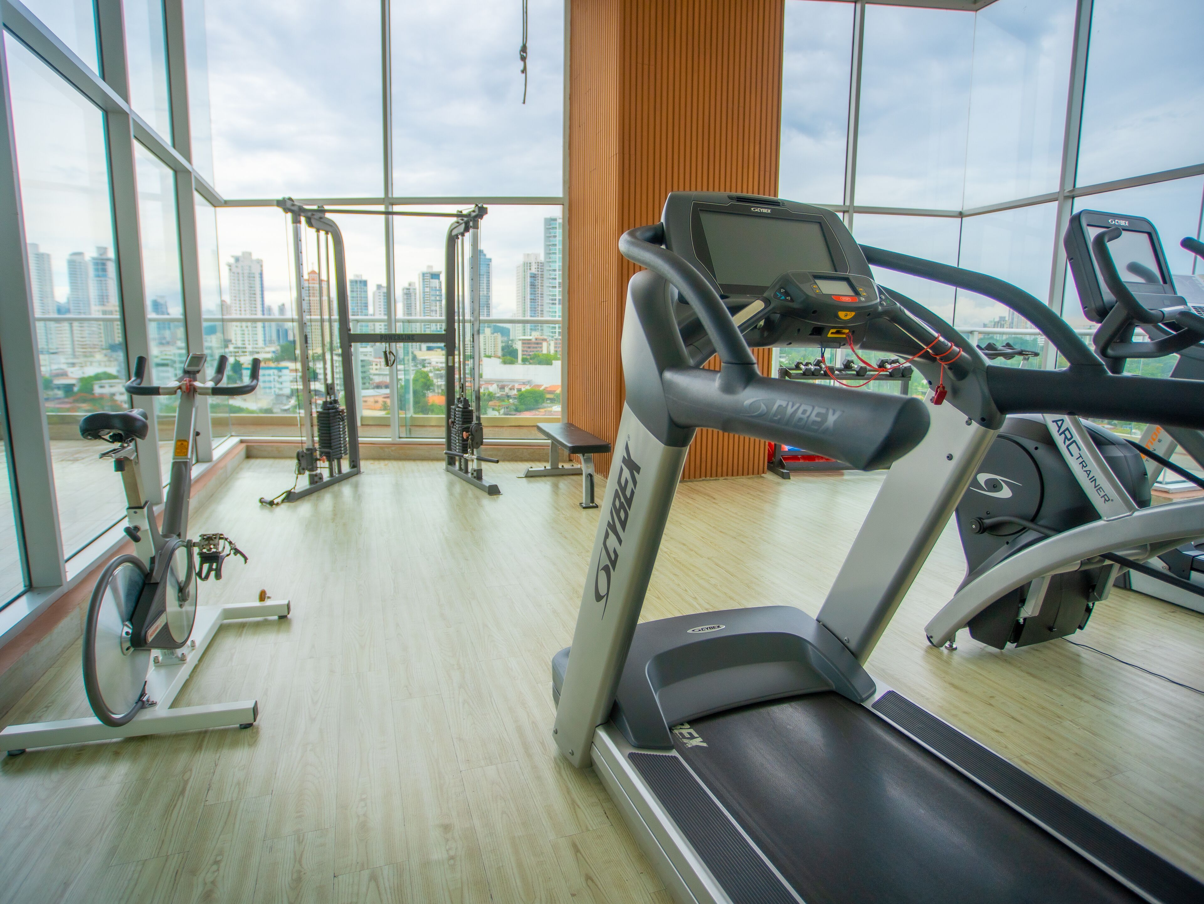 A gym with cardio machines, weight equipment, and large windows offering a city view.