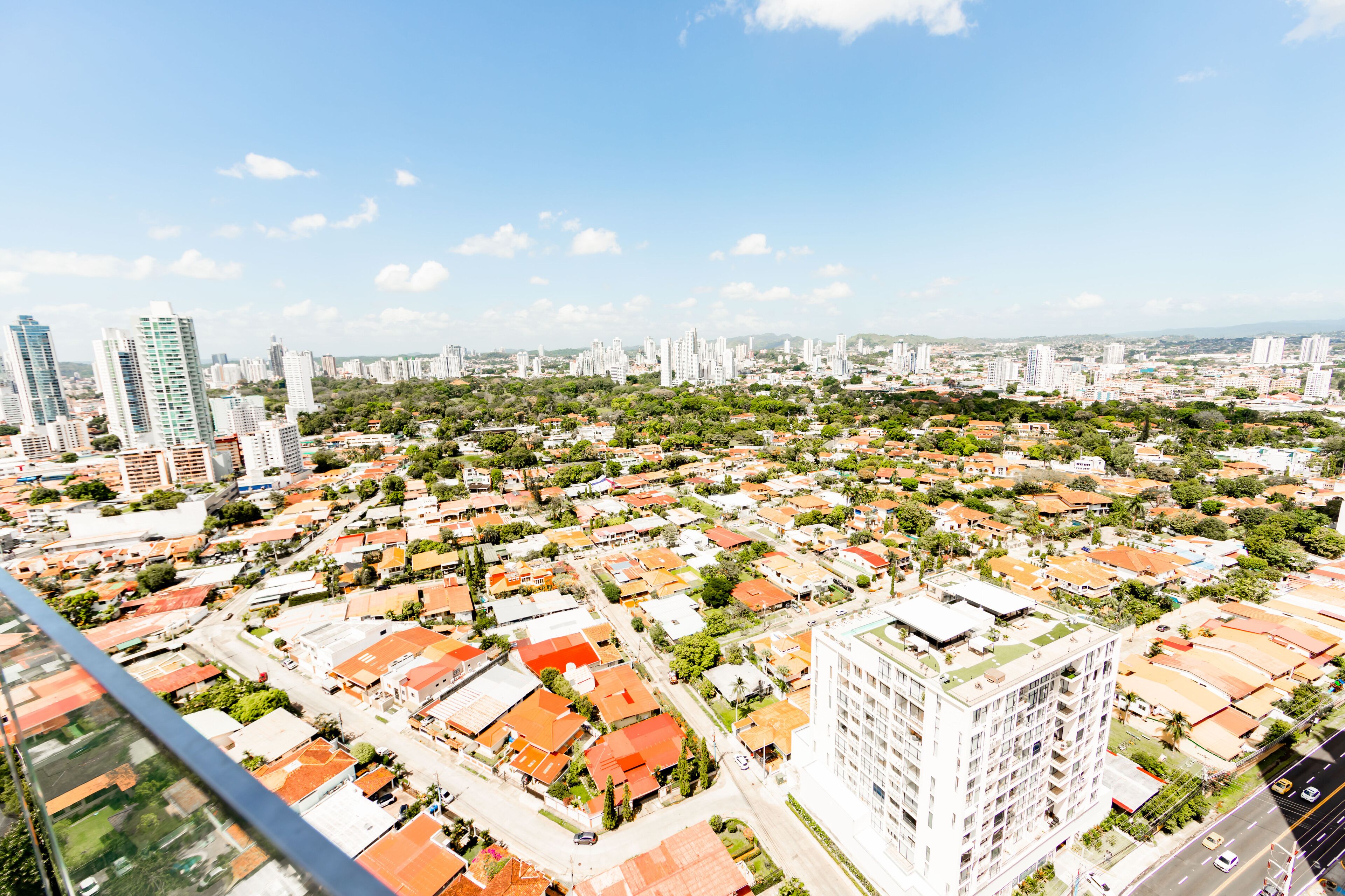 Un edificio de gran altura con varios pisos, rodeado por una zona urbana densa con diferentes edificios y áreas verdes.