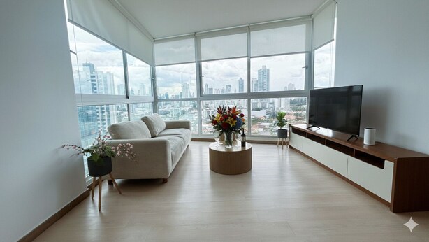 A modern living room with a sofa, a coffee table with flowers, a TV, and a large window with a city view. - Boutique Apartments Panamá Coco del Mar (Panama City)