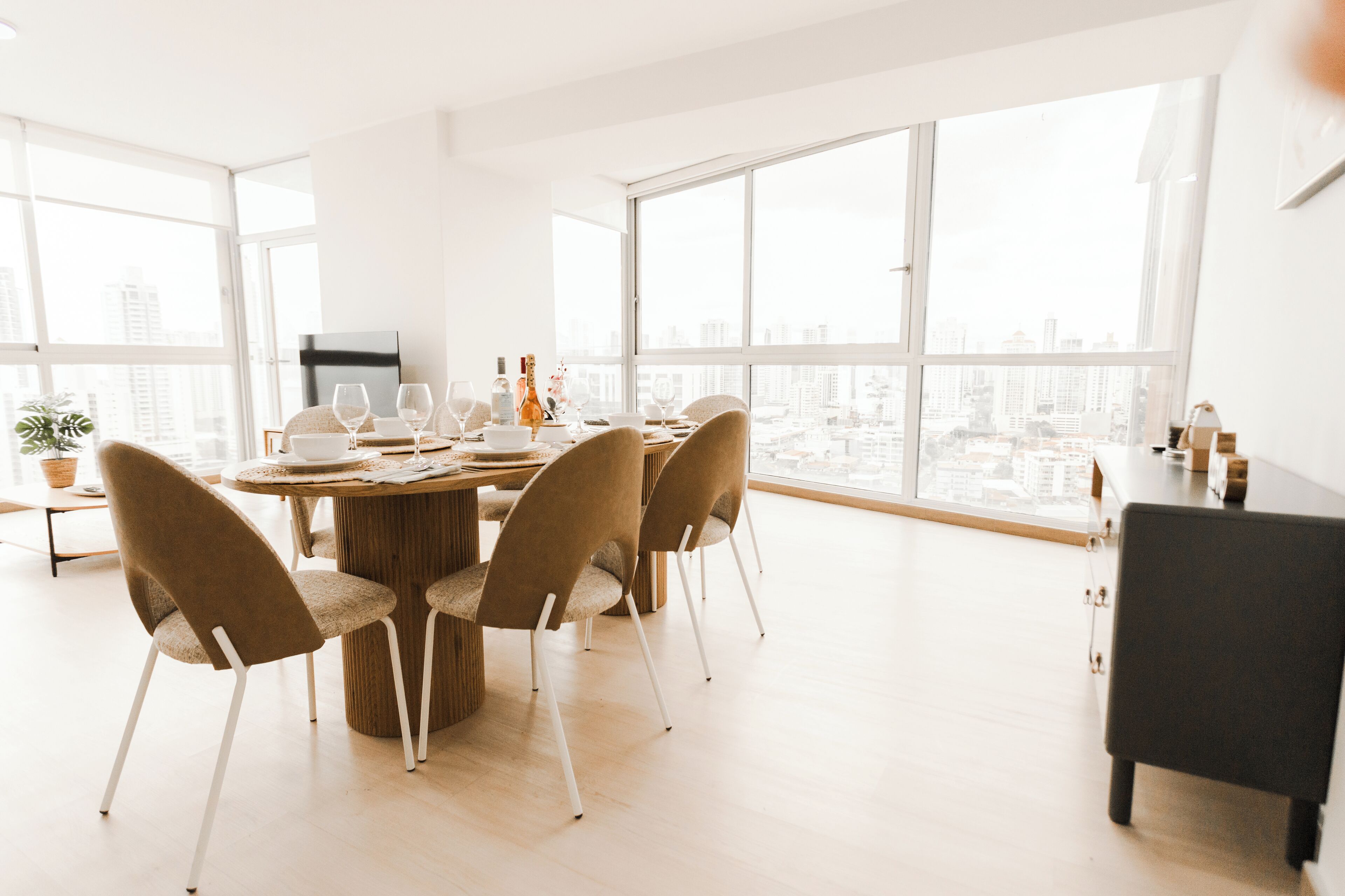 Un comedor moderno con una mesa redonda, cuatro sillas y vistas a la ciudad a través de amplias ventanas.