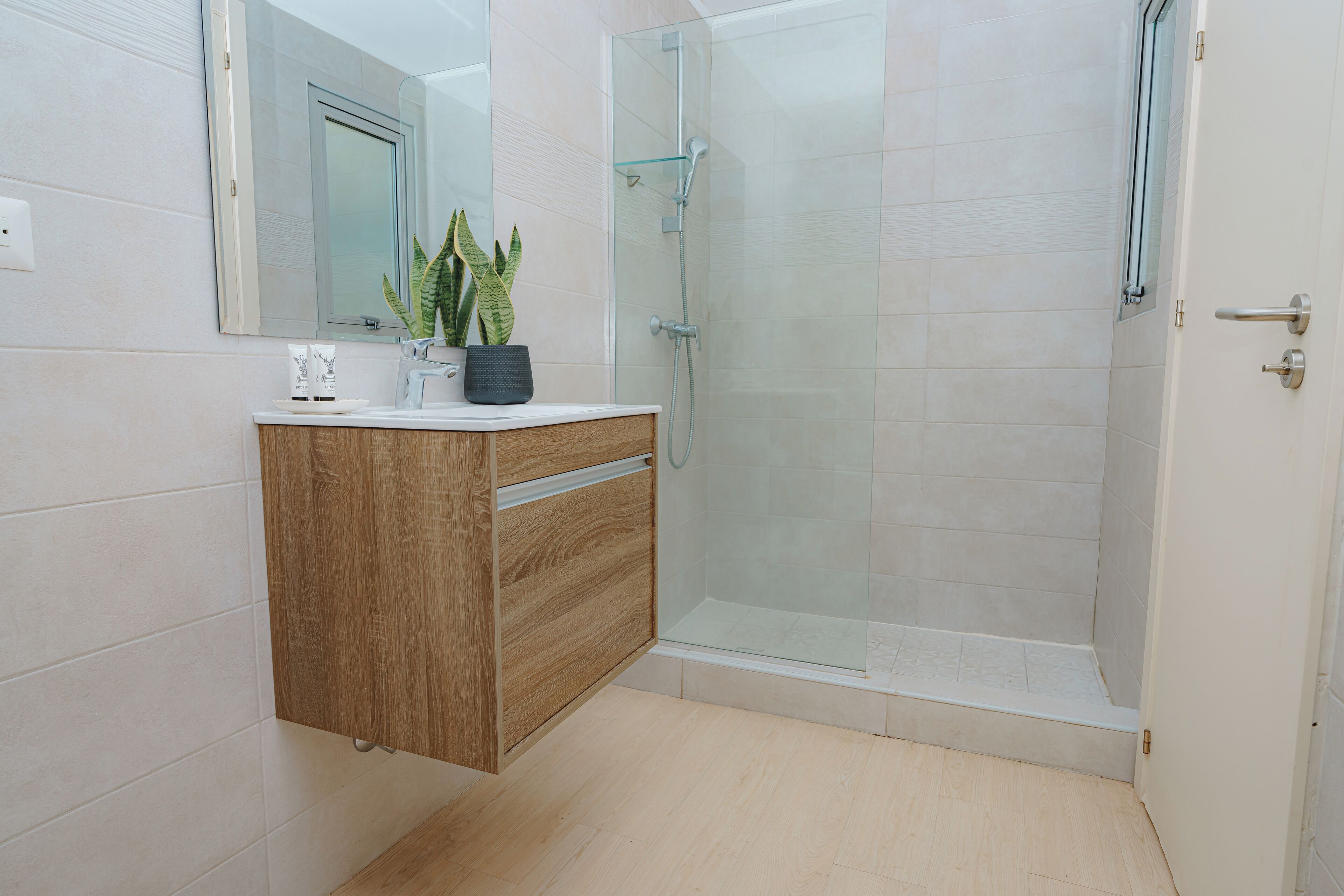 Une salle de bain moderne avec un meuble-lavabo en bois, une cabine de douche en verre et une plante en pot.