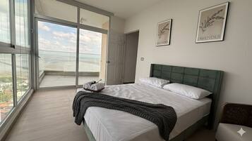 A bedroom with a large bed, a view through a glass door to the outside, and two framed pictures on the wall.