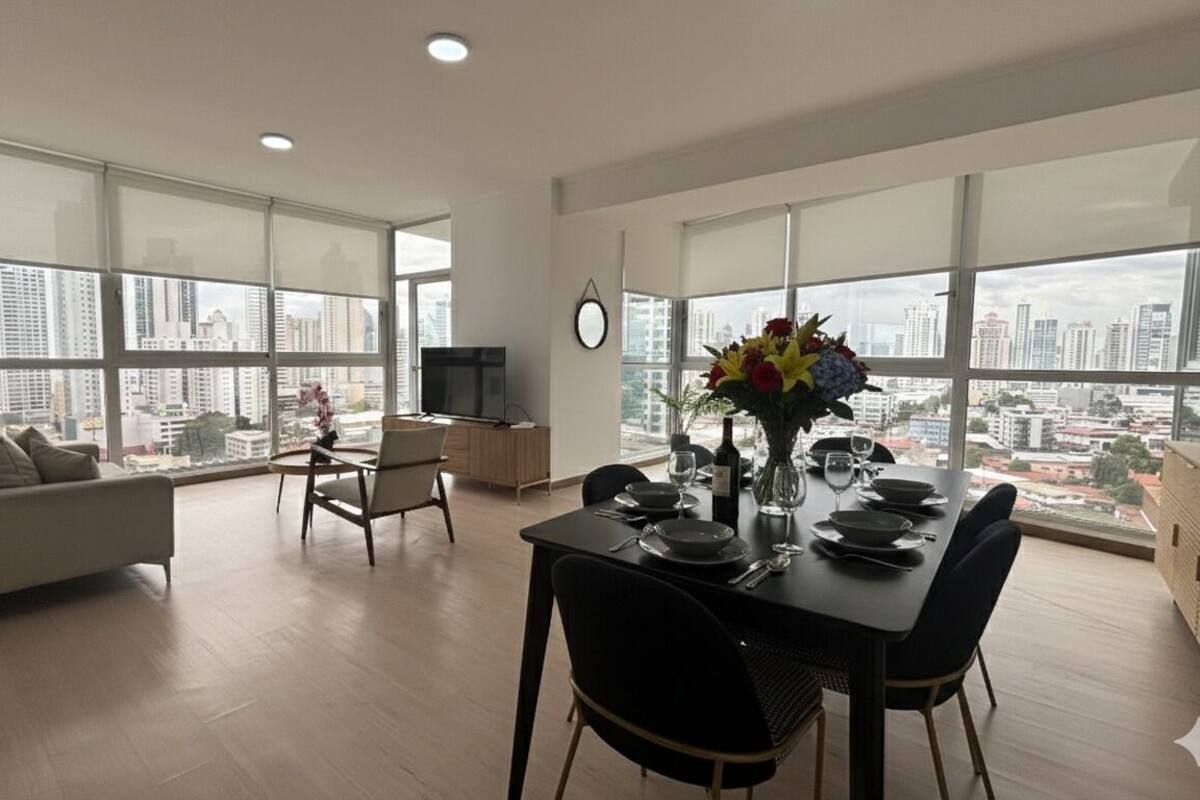 Ein modernes Wohnzimmer mit Essbereich, großen Fenstern und Blick auf die Stadt.