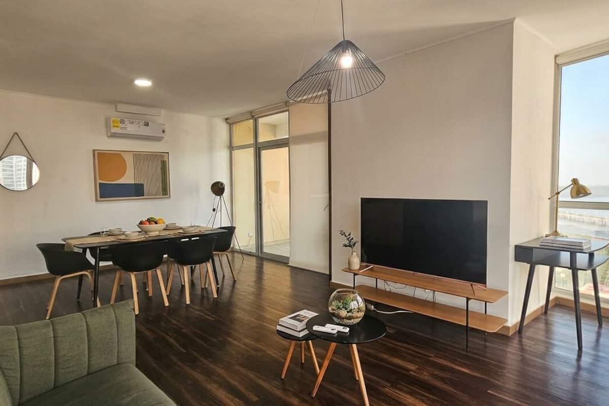 Ein modernes Wohnzimmer mit großem Fernseher, Essbereich und Blick auf eine Brücke.