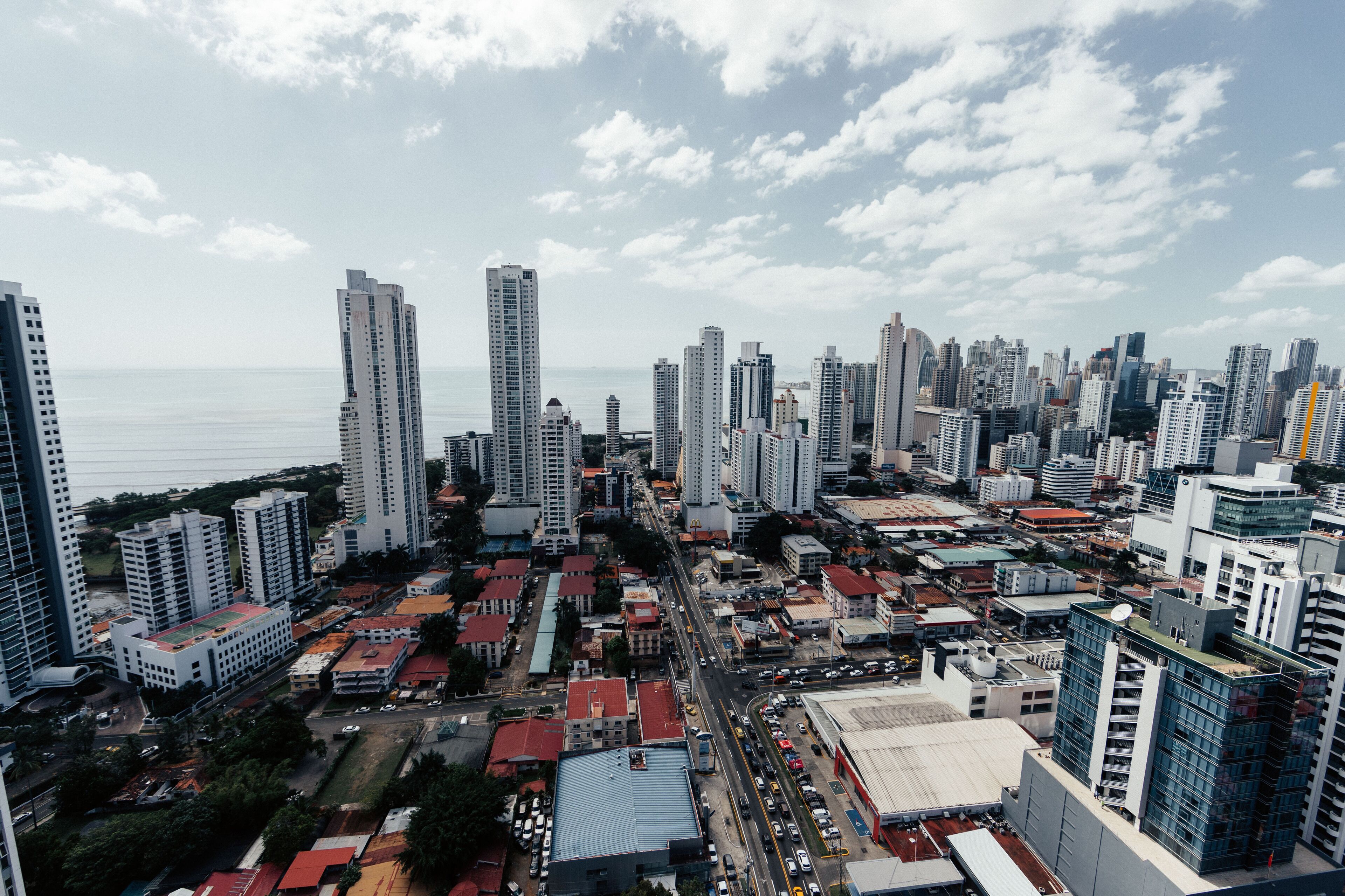 A cityscape with high-rise buildings, a busy street, and a body of water in the background.