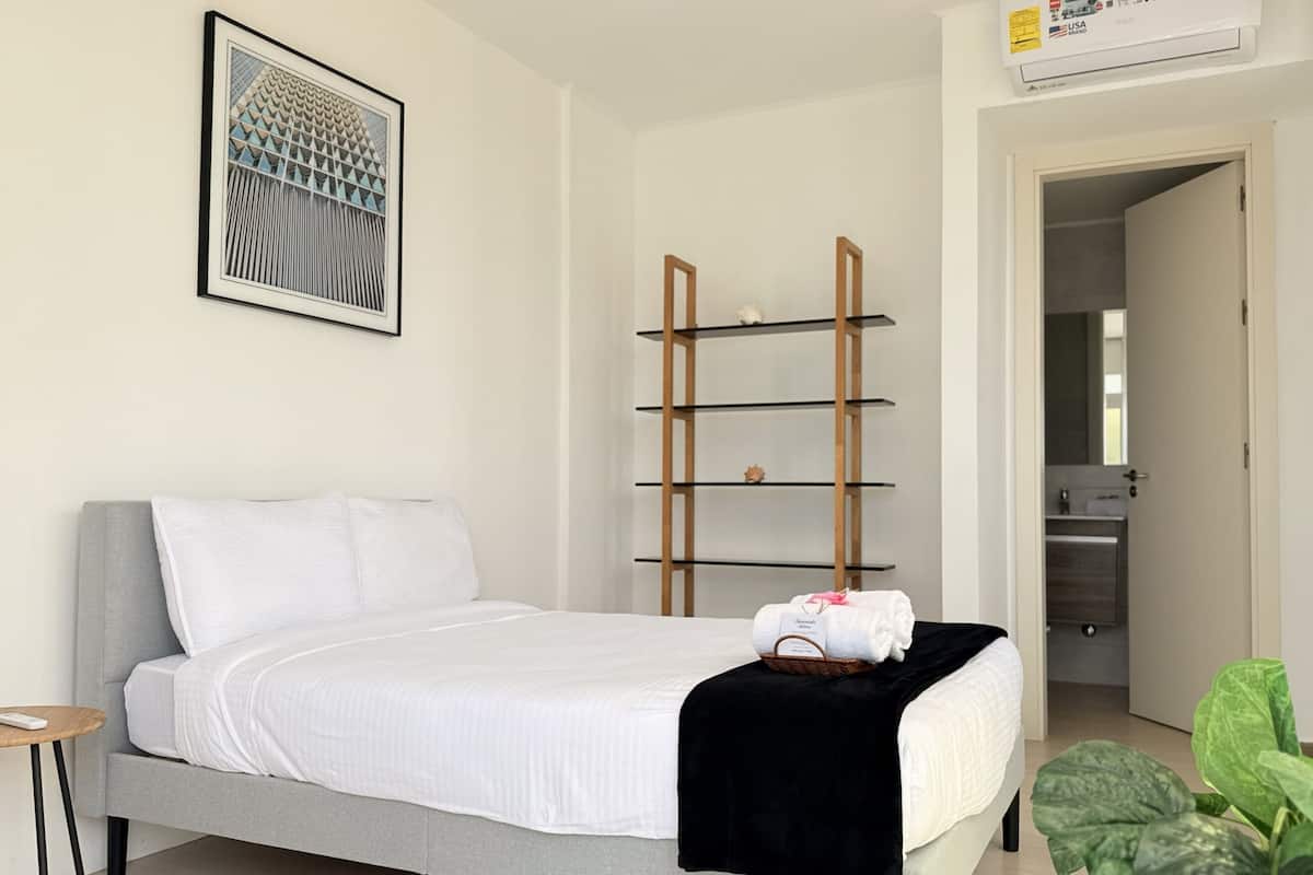 Ein modernes Schlafzimmer mit einem Bett, einem gerahmten Kunstwerk, einem Holzregal und einer Pflanze.