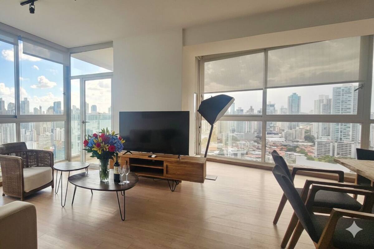 Ein großzügiges Wohnzimmer mit großem Fernseher, bequemen Sitzmöglichkeiten und Blick auf die Stadt.