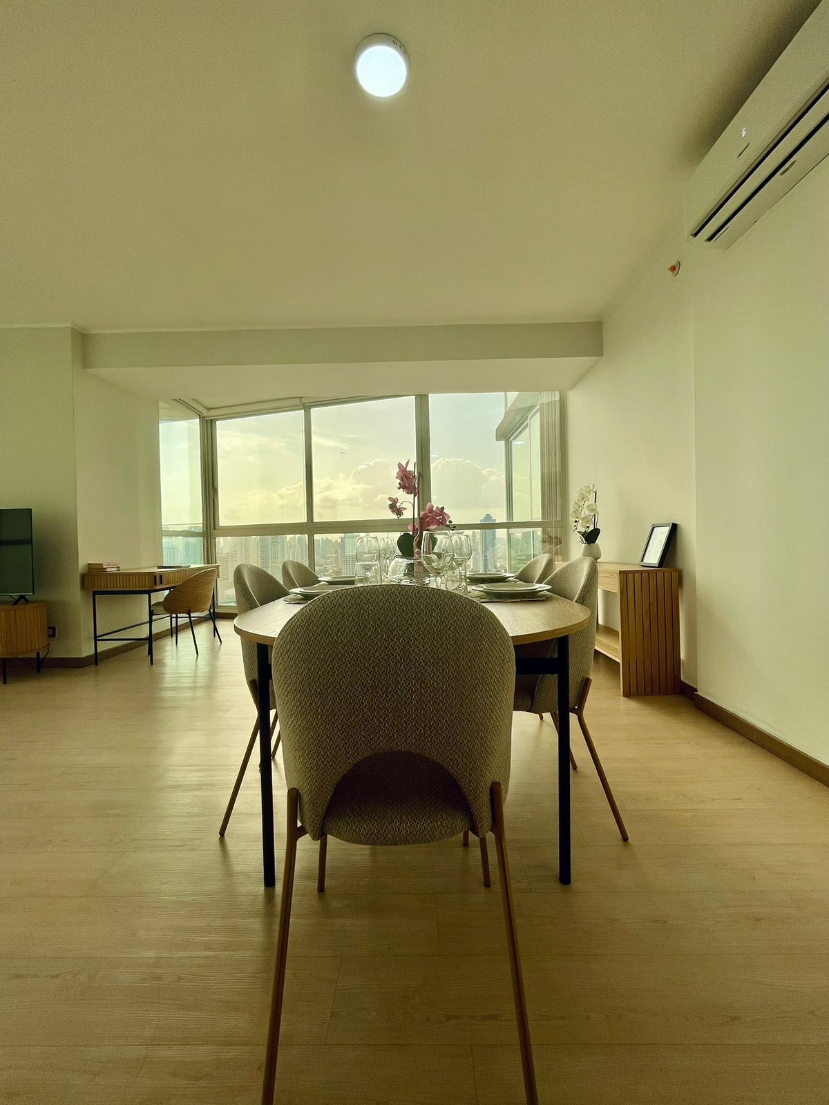 A spacious room with a large window, a dining table set for four, and a view of the city skyline.