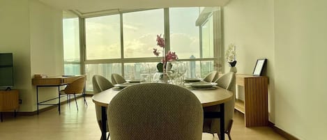 A spacious room with a large window, a dining table set for four, and a view of the city skyline.