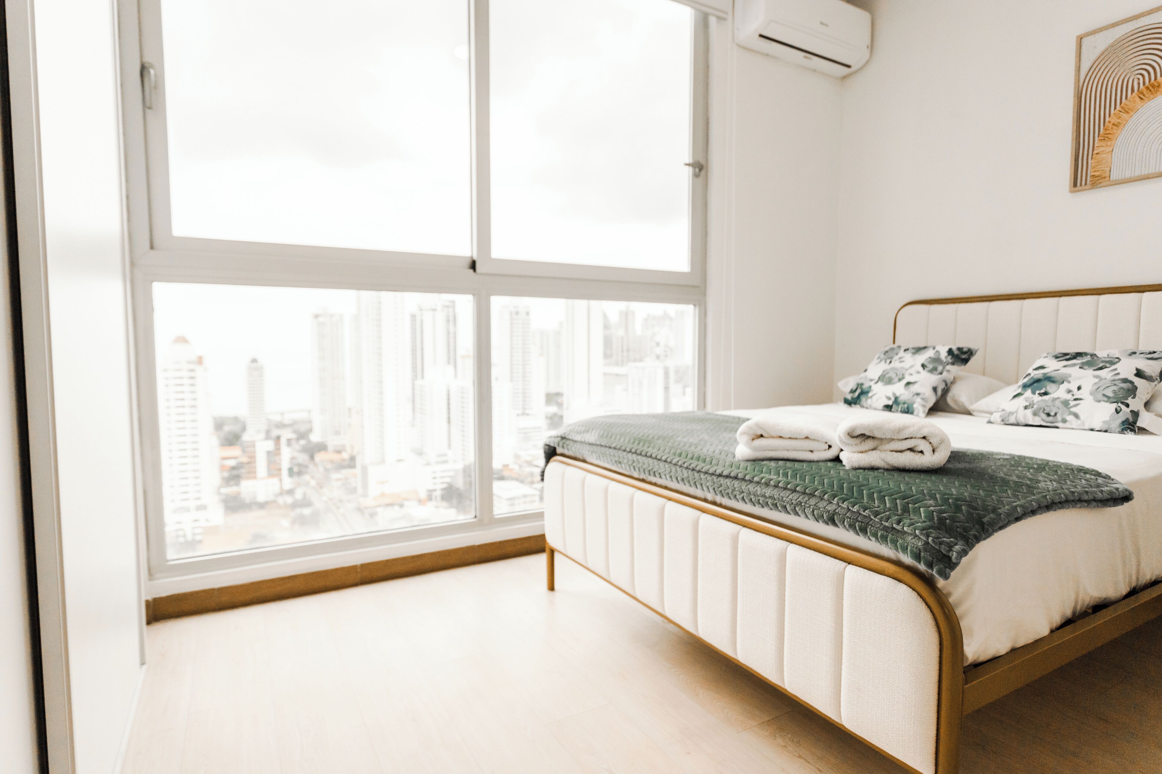 Un dormitorio con un ventanal grande, una cama con una colcha verde y vistas a la ciudad.