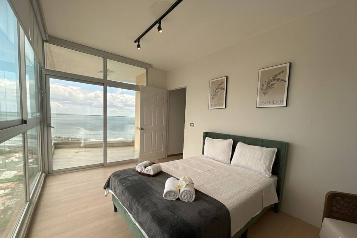 Ein Schlafzimmer mit einem großen Bett, Blick durch eine Schiebetür auf einen Balkon und zwei gerahmte Bilder an der Wand.