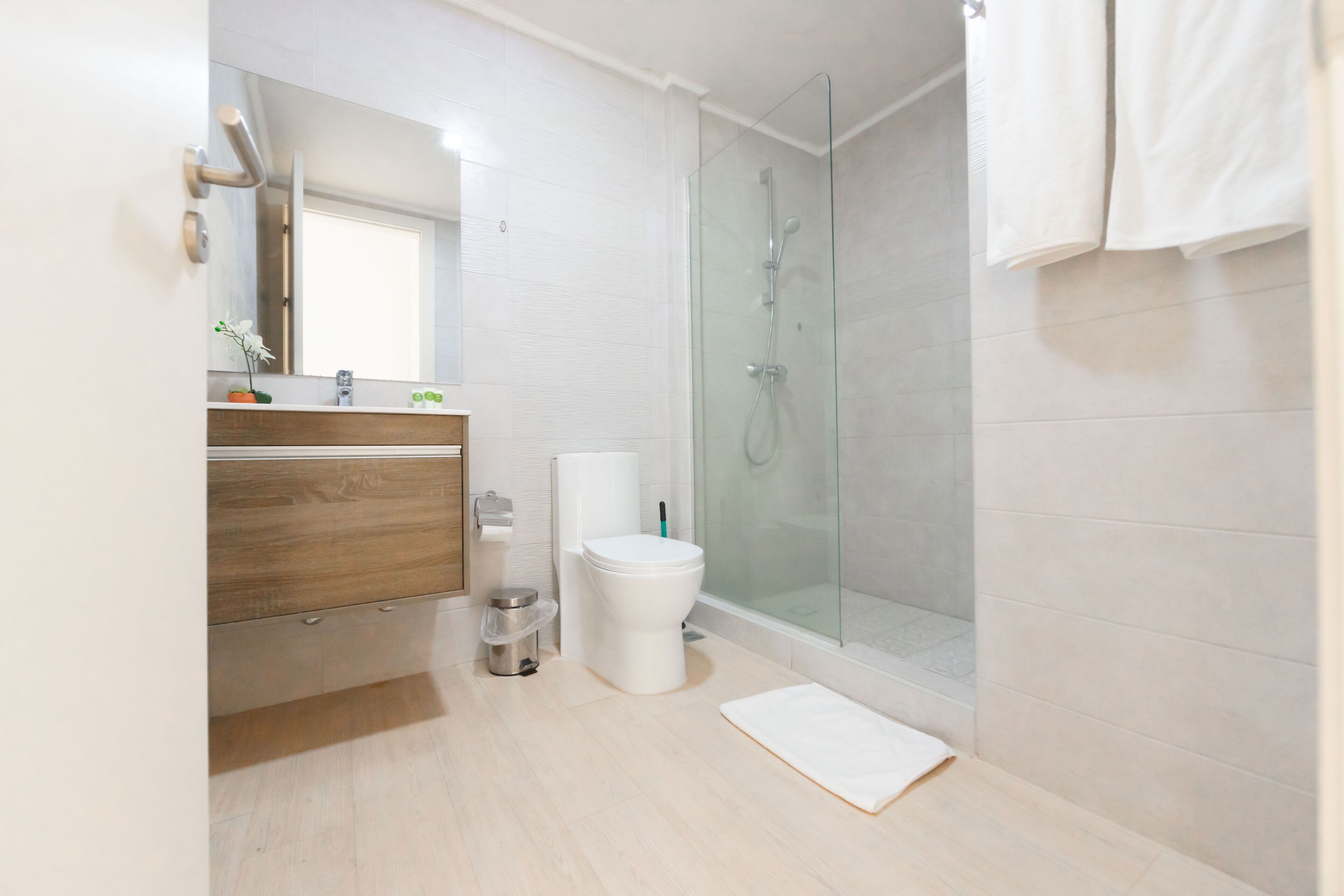 Un baño moderno con cabina de ducha de vidrio, inodoro blanco y tocador de madera.