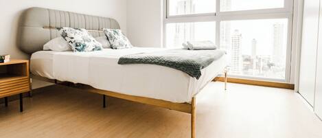 Un dormitorio moderno con un ventanal grande, una cama con cabecera gris y una mesita de noche de madera.