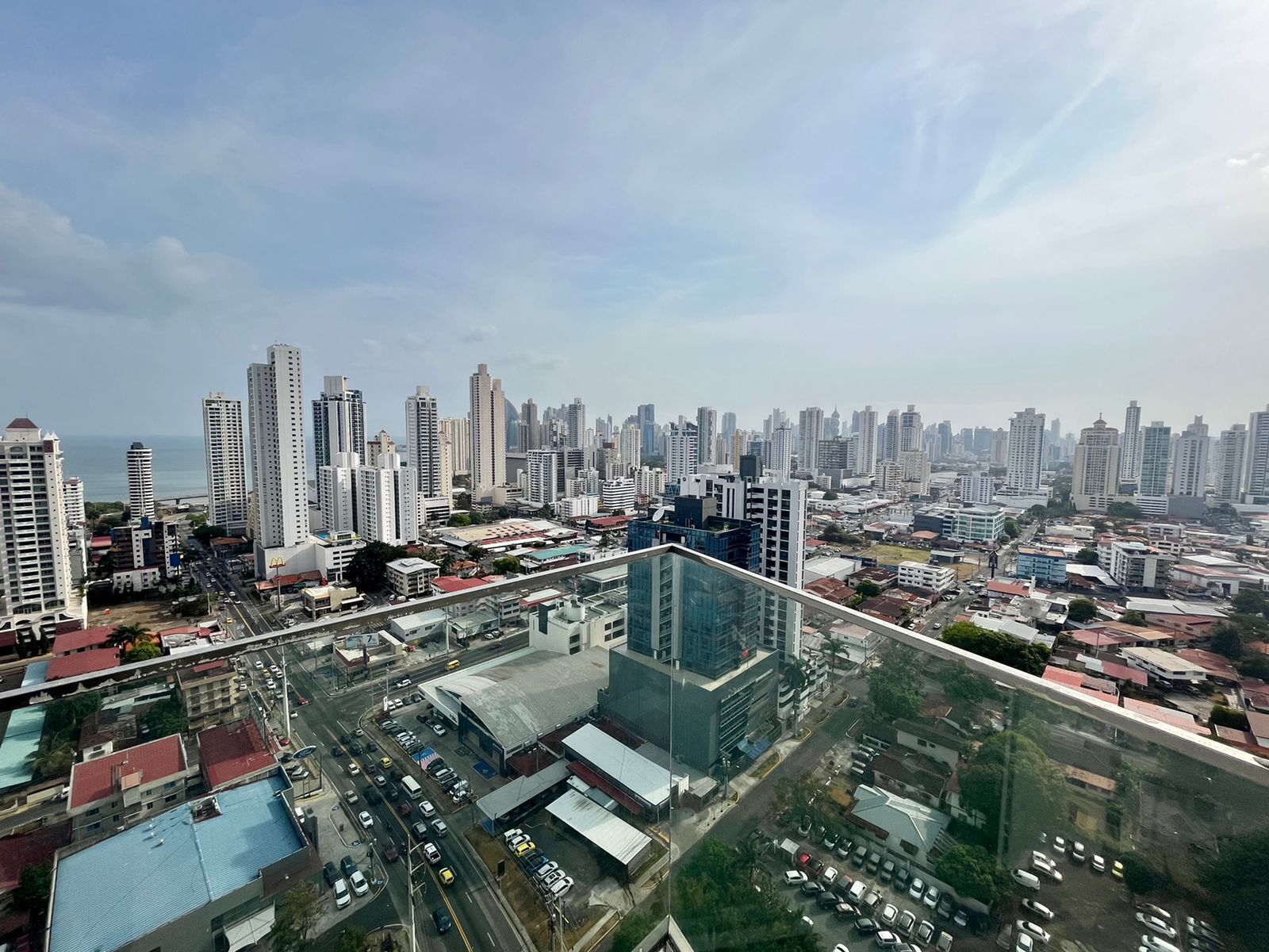 A high-rise building with a modern glass facade overlooking a cityscape with numerous high-rise buildings and a body of water in the distance.
