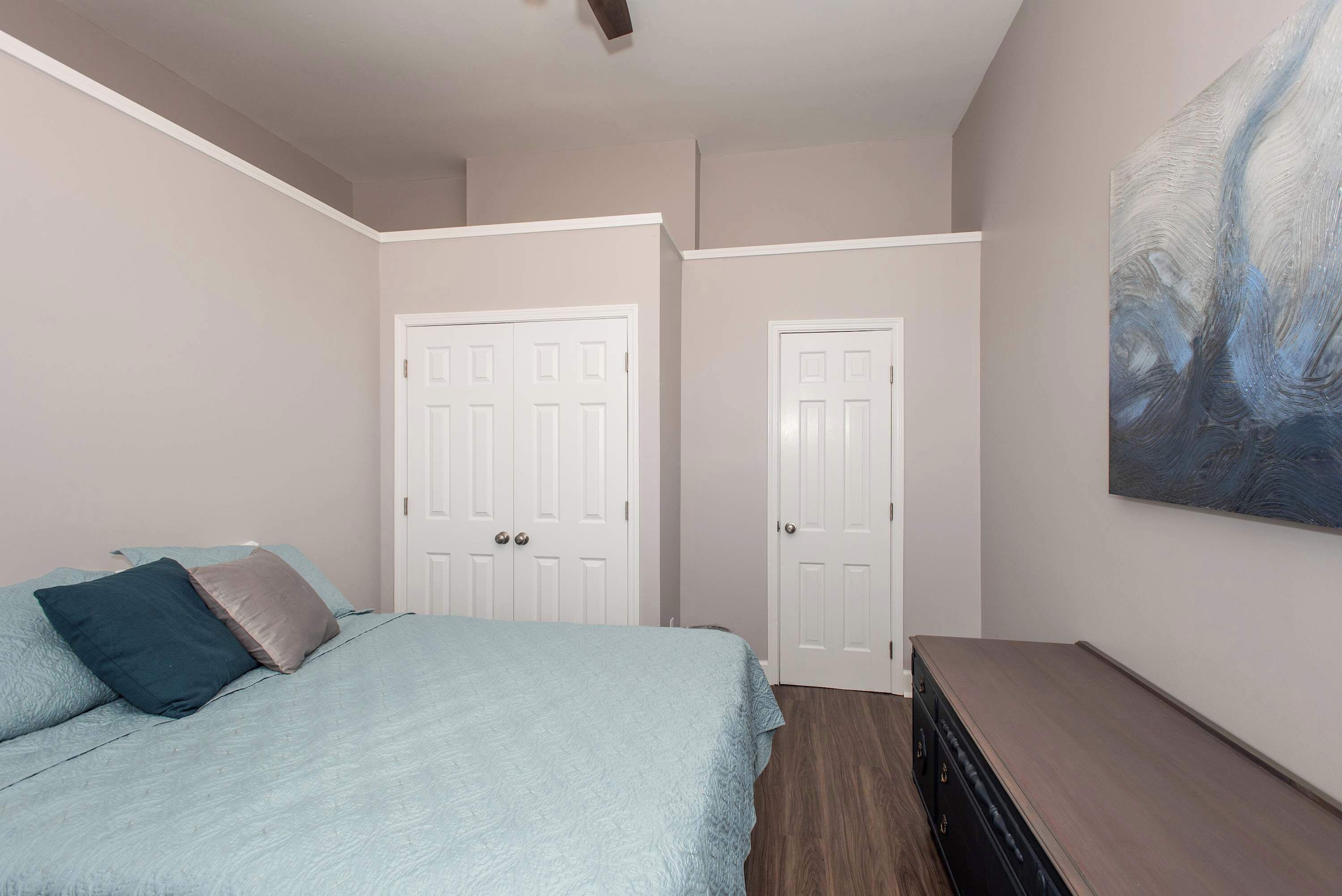 A bedroom with a bed, two doors, a dresser, and a painting on the wall.