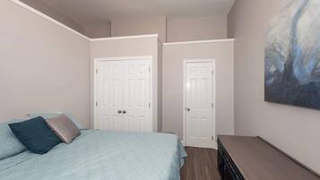 A bedroom with a bed, two doors, a dresser, and a painting on the wall.