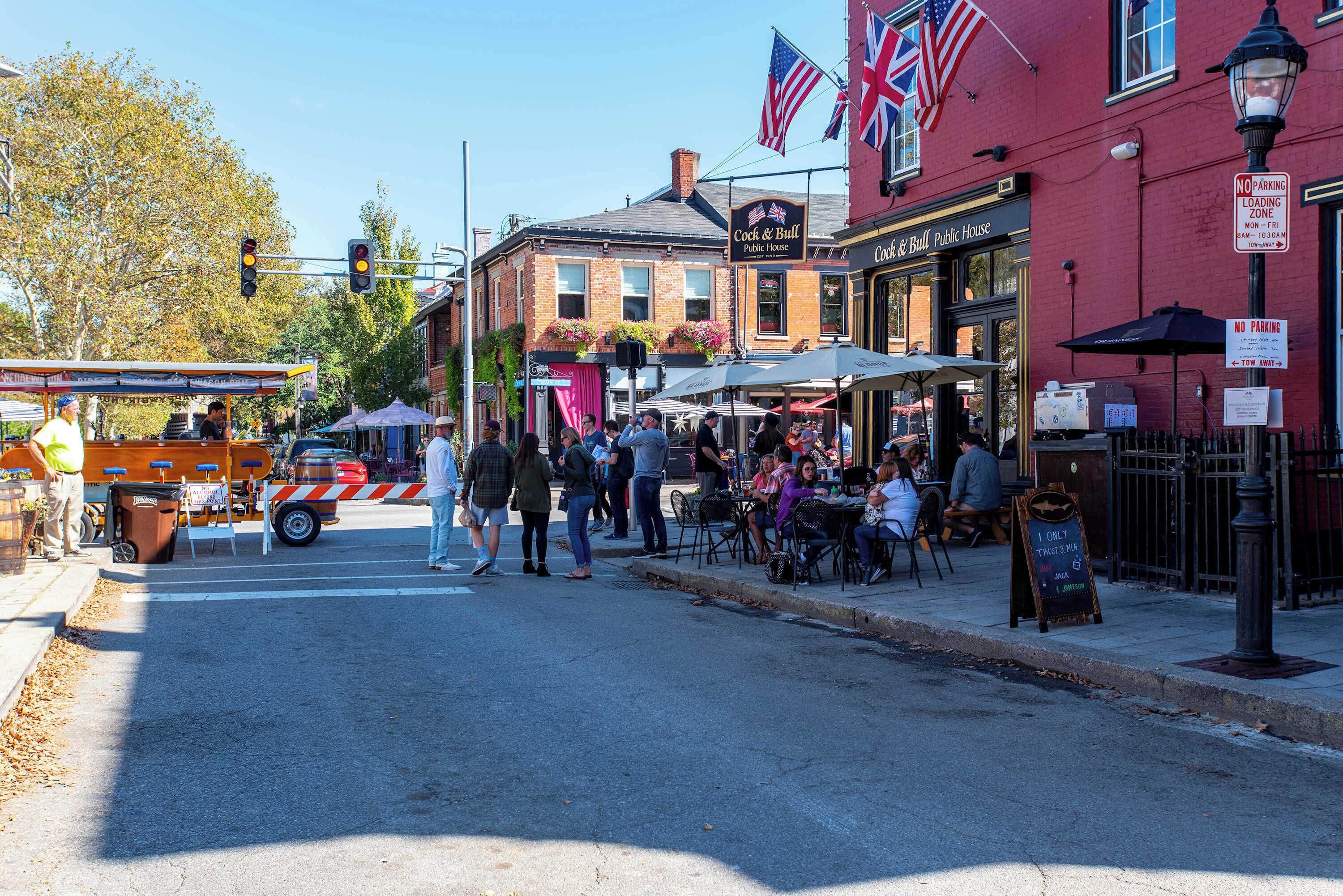 A street scene with outdoor seating at a pub, a red building with flags, and a no parking sign.
