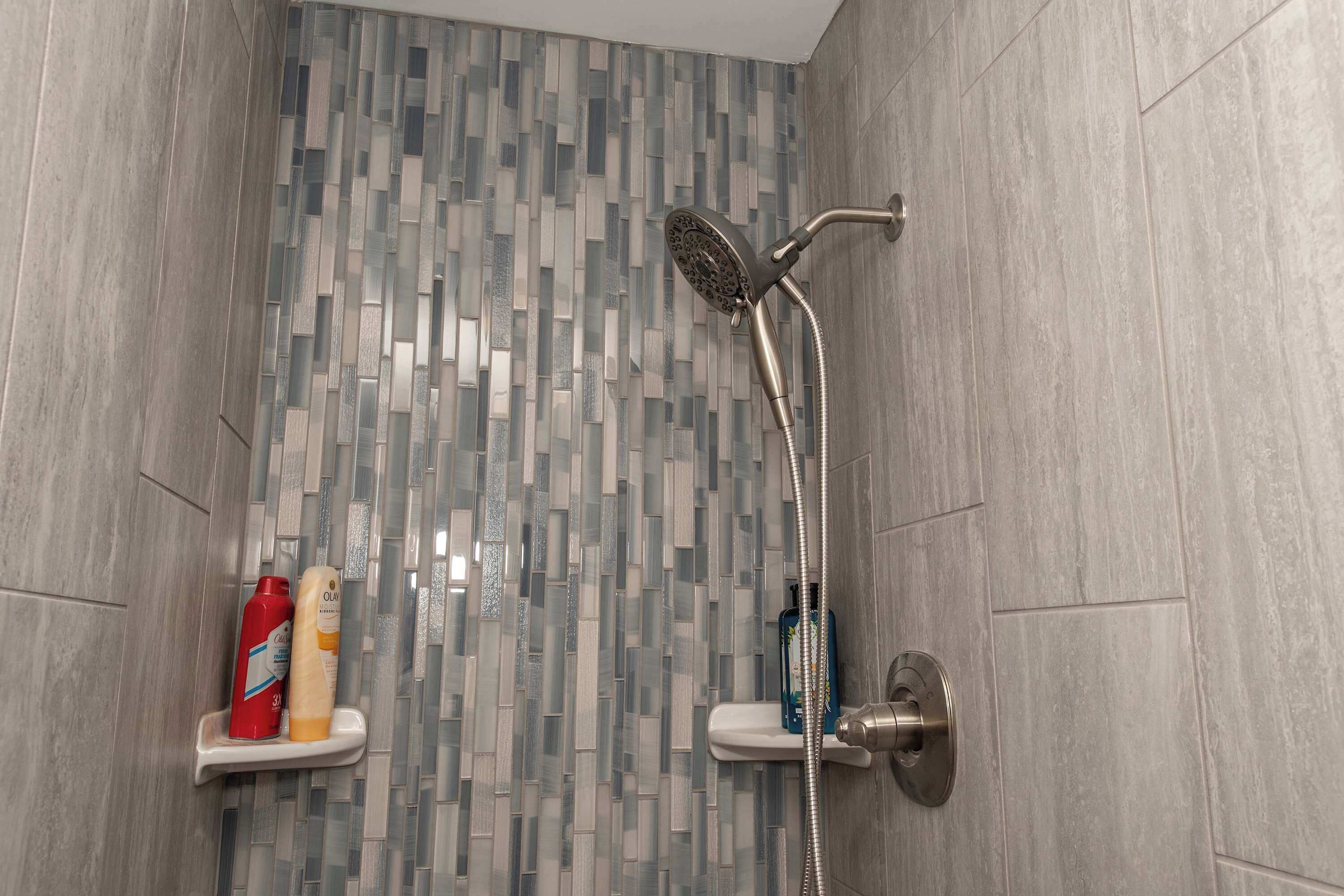 Een douche met een modern design, met een wand betegeld met mozaïek en een handdouche.