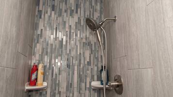 Een douche met een modern design, met een wand betegeld met mozaïek en een handdouche.