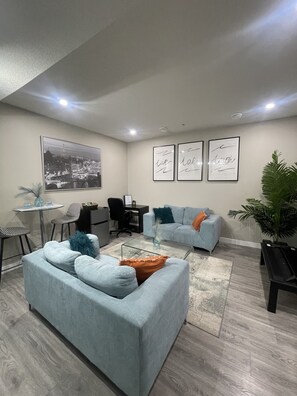Relax in this stylish living room with a sofa, coffee table, and chairs, surrounded by a cityscape artwork and lush greenery.