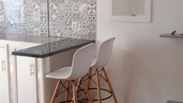 Moderni keittiö, jossa on valkoiset kaapit, marmorista tehty välitila ja ruokailualue, jossa on valkoinen tuoli ja rahi.
