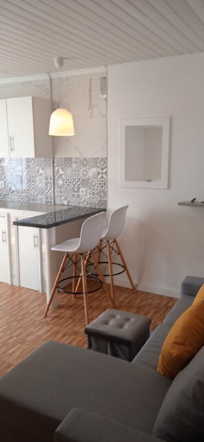 A modern kitchen with white cabinets, a marble backsplash, and a dining area with a white chair and ottoman. - Great place (Arrifes)