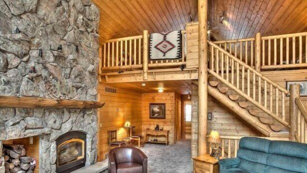 A log cabin interior with a stone fireplace, a wooden staircase, a blue sofa, and a wooden chair. - Beautiful Log Cabin with Acreage (Estes Park)