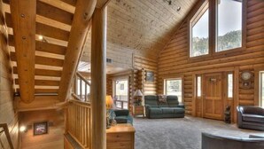 A log cabin interior with a staircase, a sofa, a coffee table, and a fireplace. - Beautiful Log Cabin with Acreage (Estes Park)