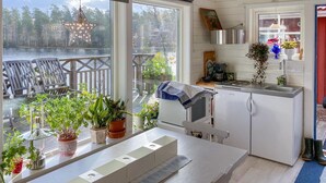 A modern kitchen with a view of a lake, wooden deck, and potted plants. - Cozy home in Bottnaryd with lake view (Bottnaryd)