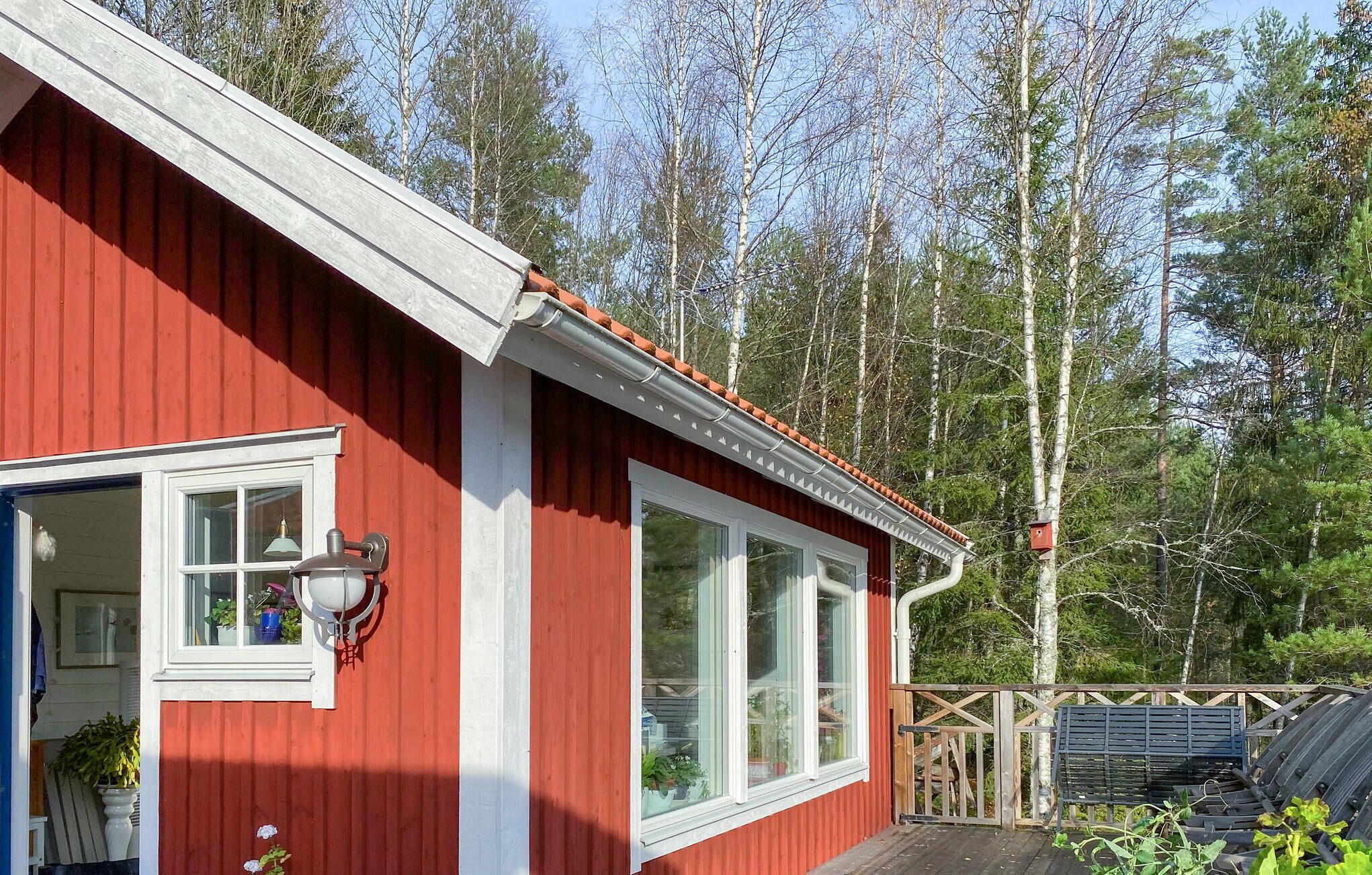 Eine rote Holzhütte mit weißem Zierdekor, großen Fenstern und einer Holzterrasse.