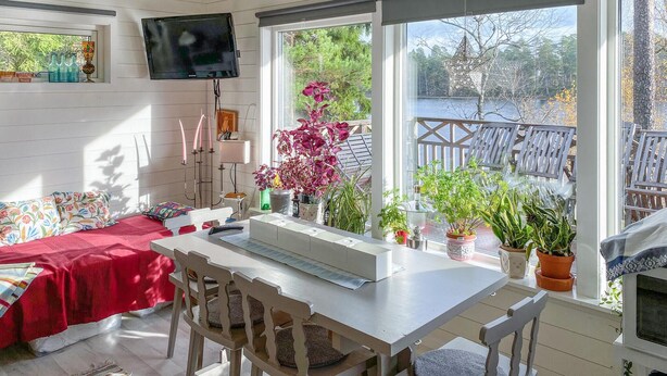 A sunlit room with a dining table, chairs, a TV mounted on the wall, and a view of a lake through large windows. - Cozy home in Bottnaryd with lake view (Bottnaryd)