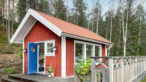 A red wooden cabin with a red-tiled roof, a blue door, and a wooden deck. - Cozy home in Bottnaryd with lake view (Bottnaryd)