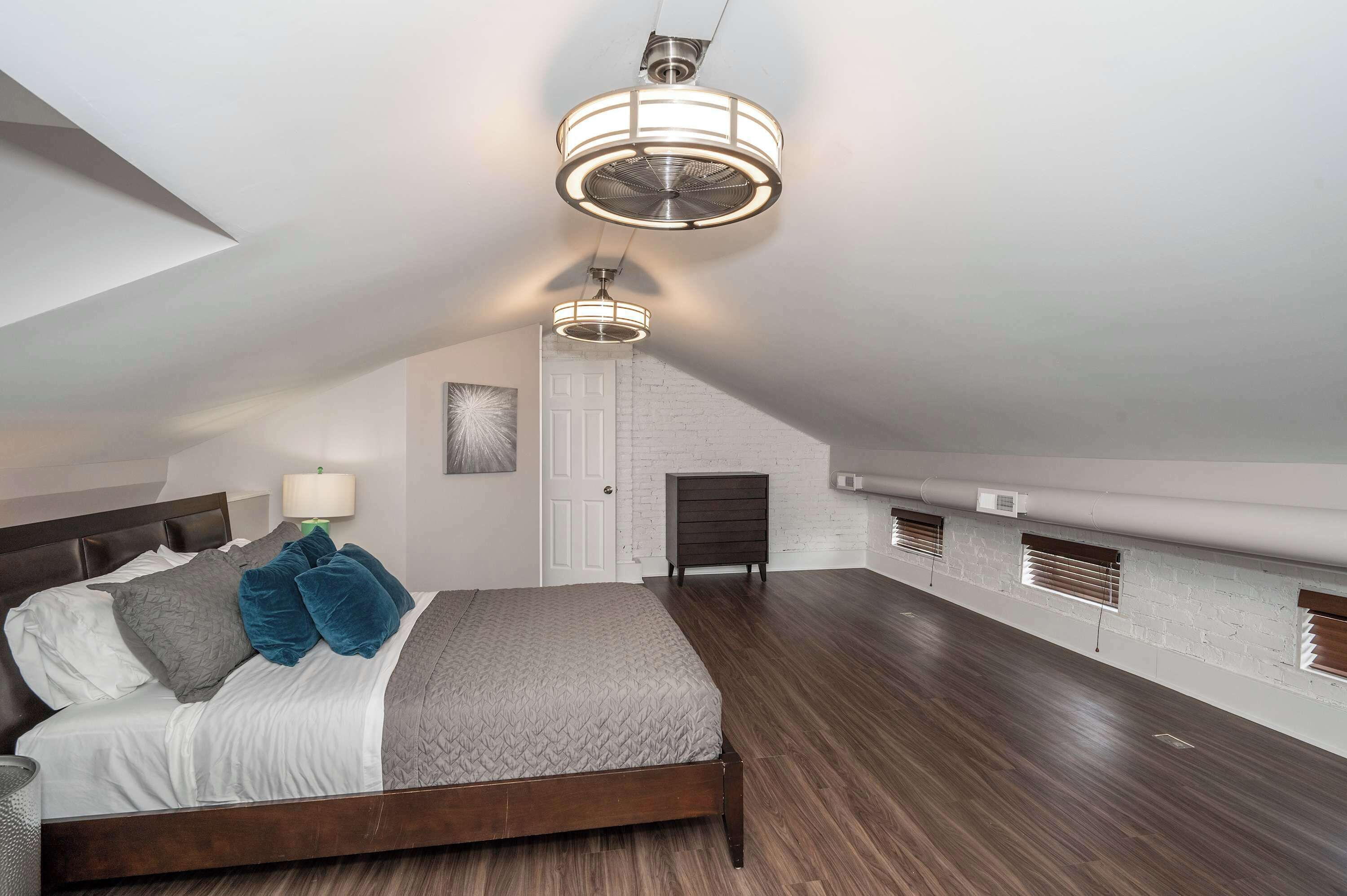 A bedroom with a sloped ceiling, a bed with a headboard, a bedside lamp, and a door.