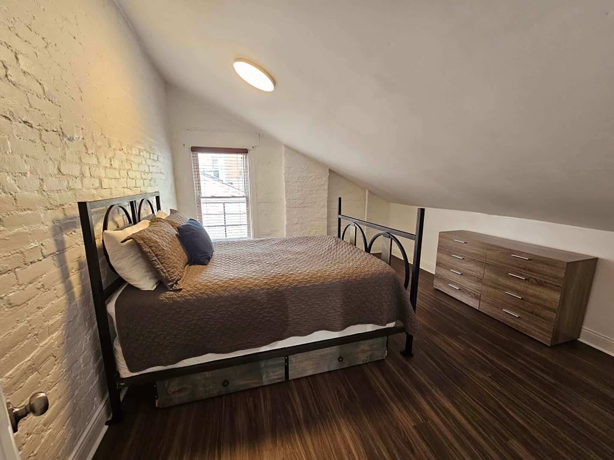 Ein Schlafzimmer mit Schlafpodest, Holzkasten, Mauerwerk und einem Fenster.