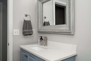 A bathroom with a white sink, a mirror with an ornate frame, a towel hanging on a rack, and a soap dispenser. - Heart of Mainstrasse 3 (Covington)