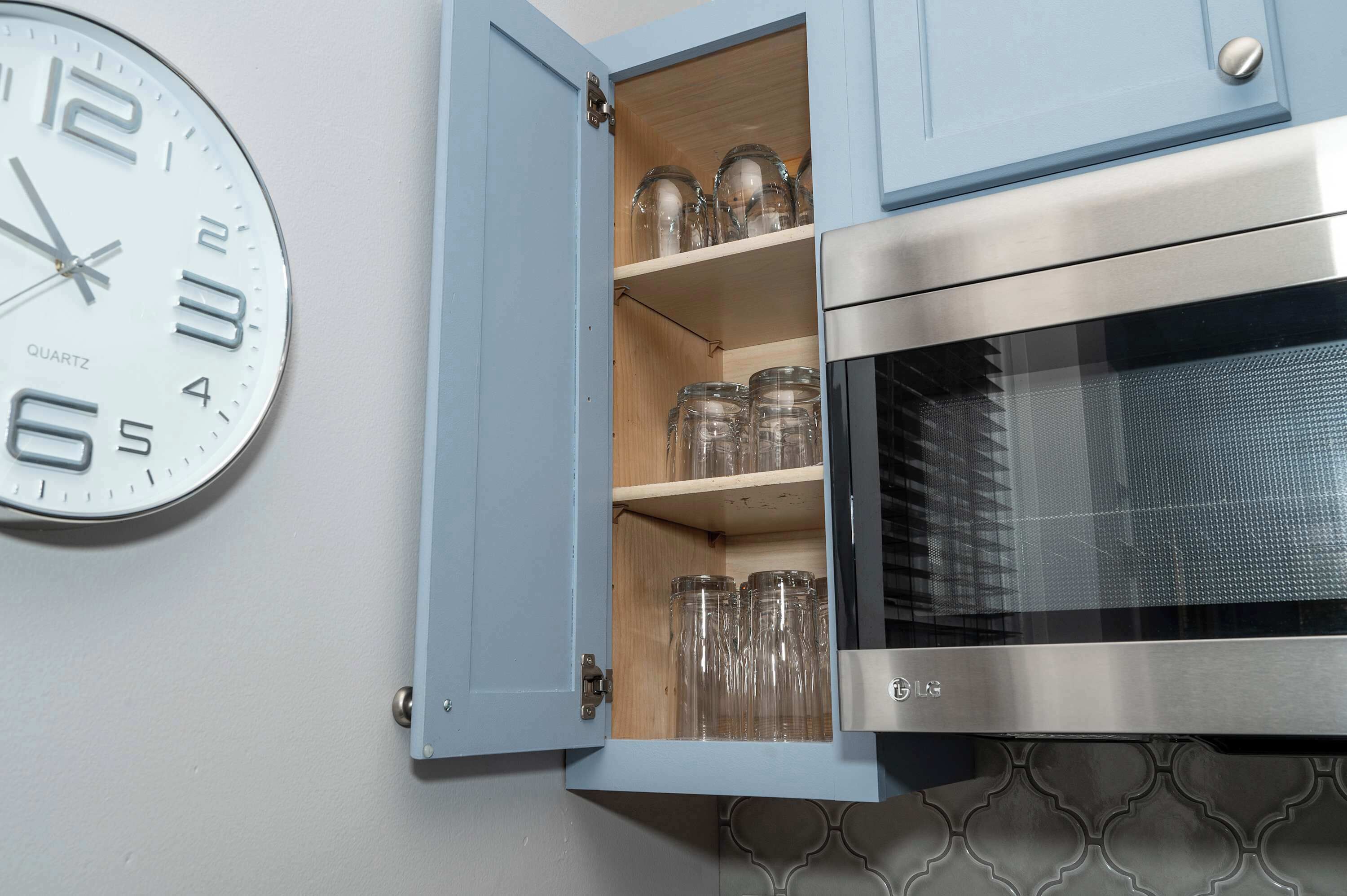 A kitchen with a quartz clock, a microwave, and a cabinet with glass jars.