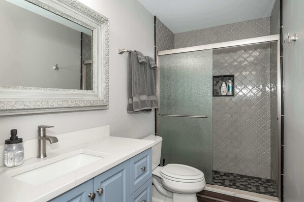 A bathroom with a white sink, a large mirror, a toilet, and a shower with a glass door. - Heart of Mainstrasse 3 (Covington)