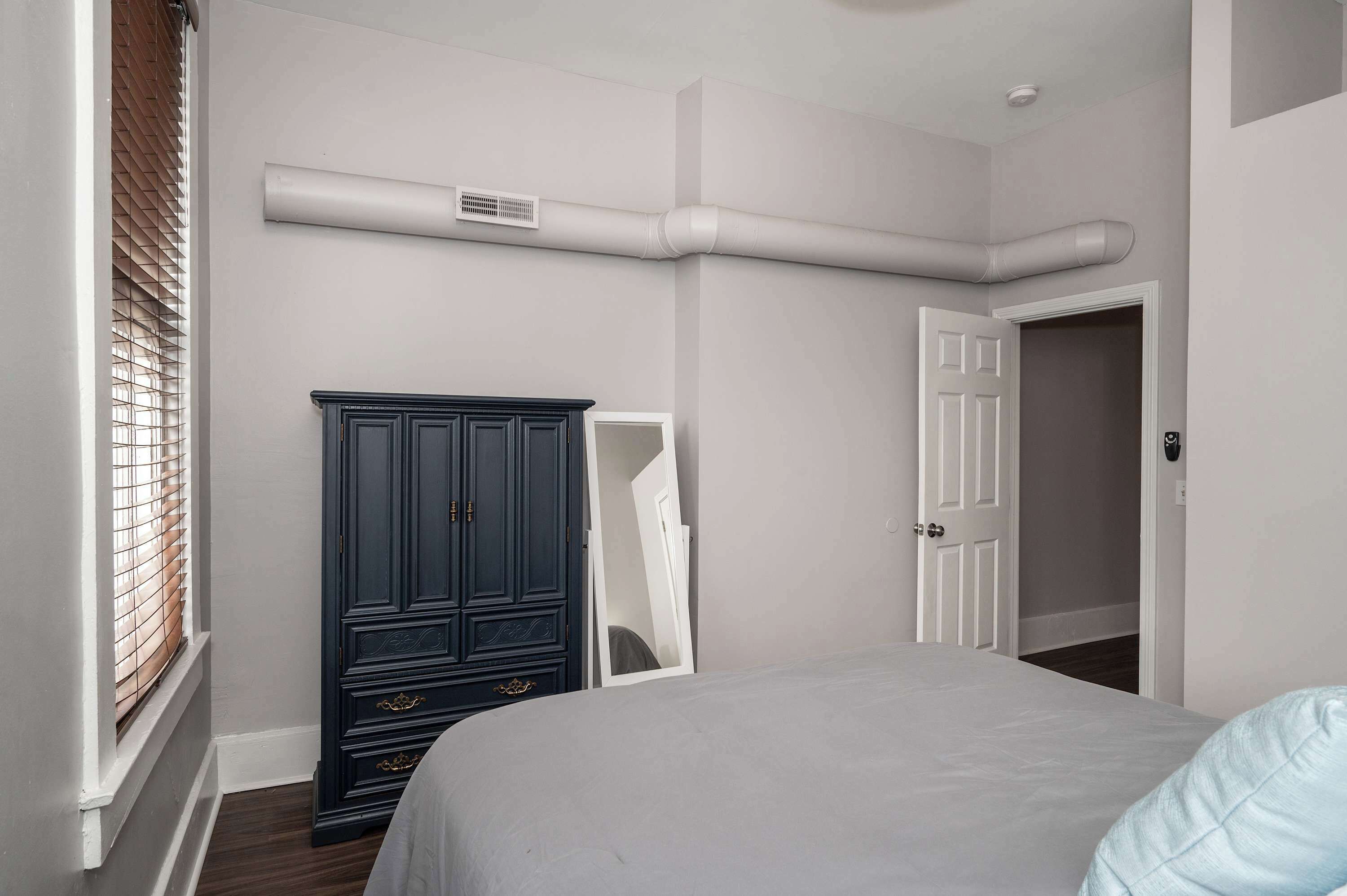 A bedroom with a bed, a dark wooden wardrobe, a white door, and a window with blinds.