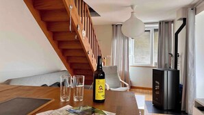 Ein gemütliches Wohnzimmer mit einer Holztreppe, einem Esstisch mit einer Weinflasche, Gläsern und einer Karte.