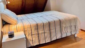 Ein kleiner, gemütlicher Raum mit schrägem Dach und Fenster. Er verfügt über ein Einzelbett mit gestreifter Bettwäsche und einen Nachttisch.