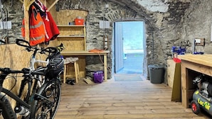 Ein rustikaler Raum mit Holzboden, einem Fahrrad, einem Tisch mit einer roten Jacke und einer zur Außenwelt führenden Tür.