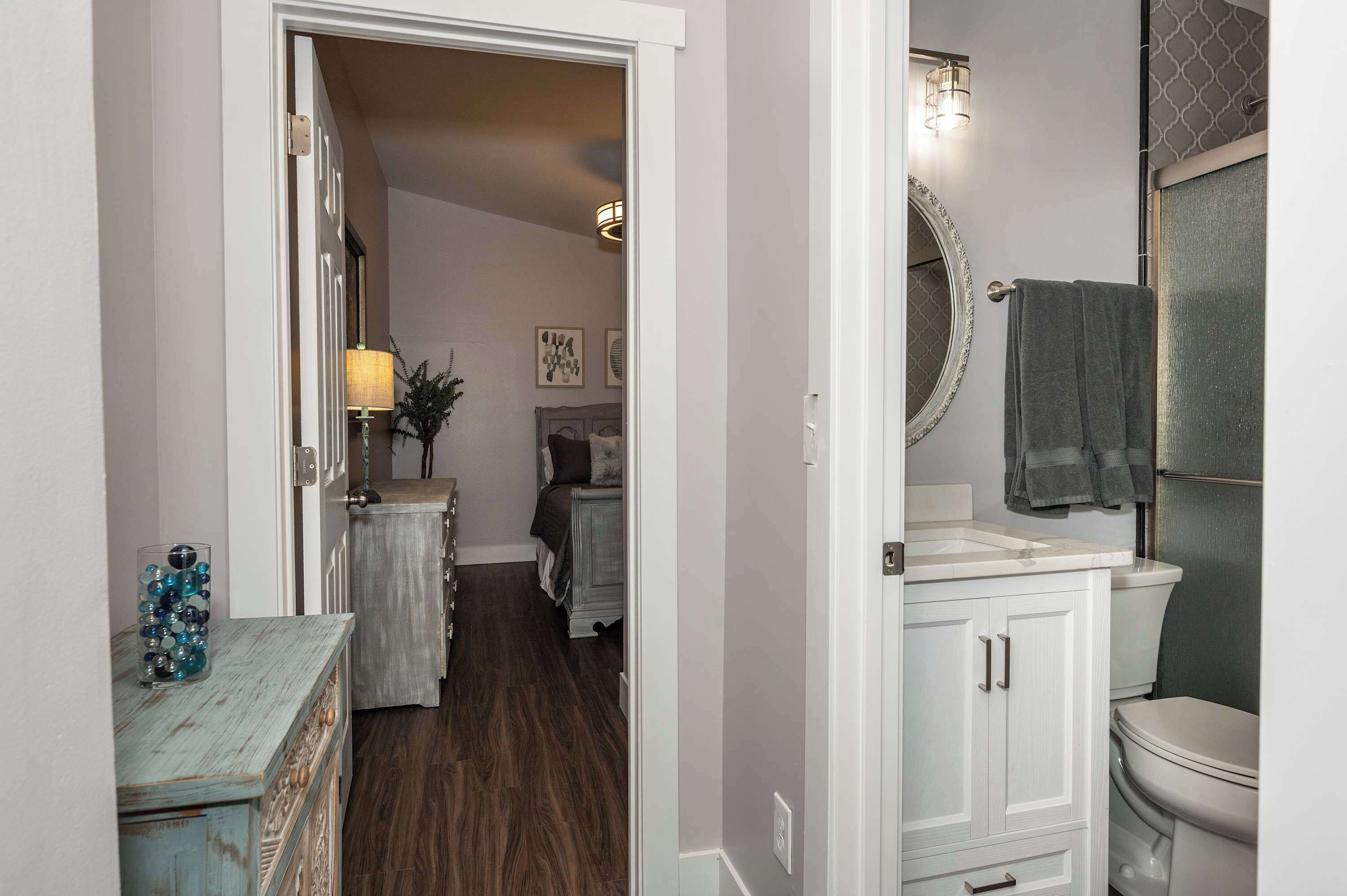 A bathroom with a toilet, sink, and mirror. There is a towel rack above the sink and a decorative vase on the counter.