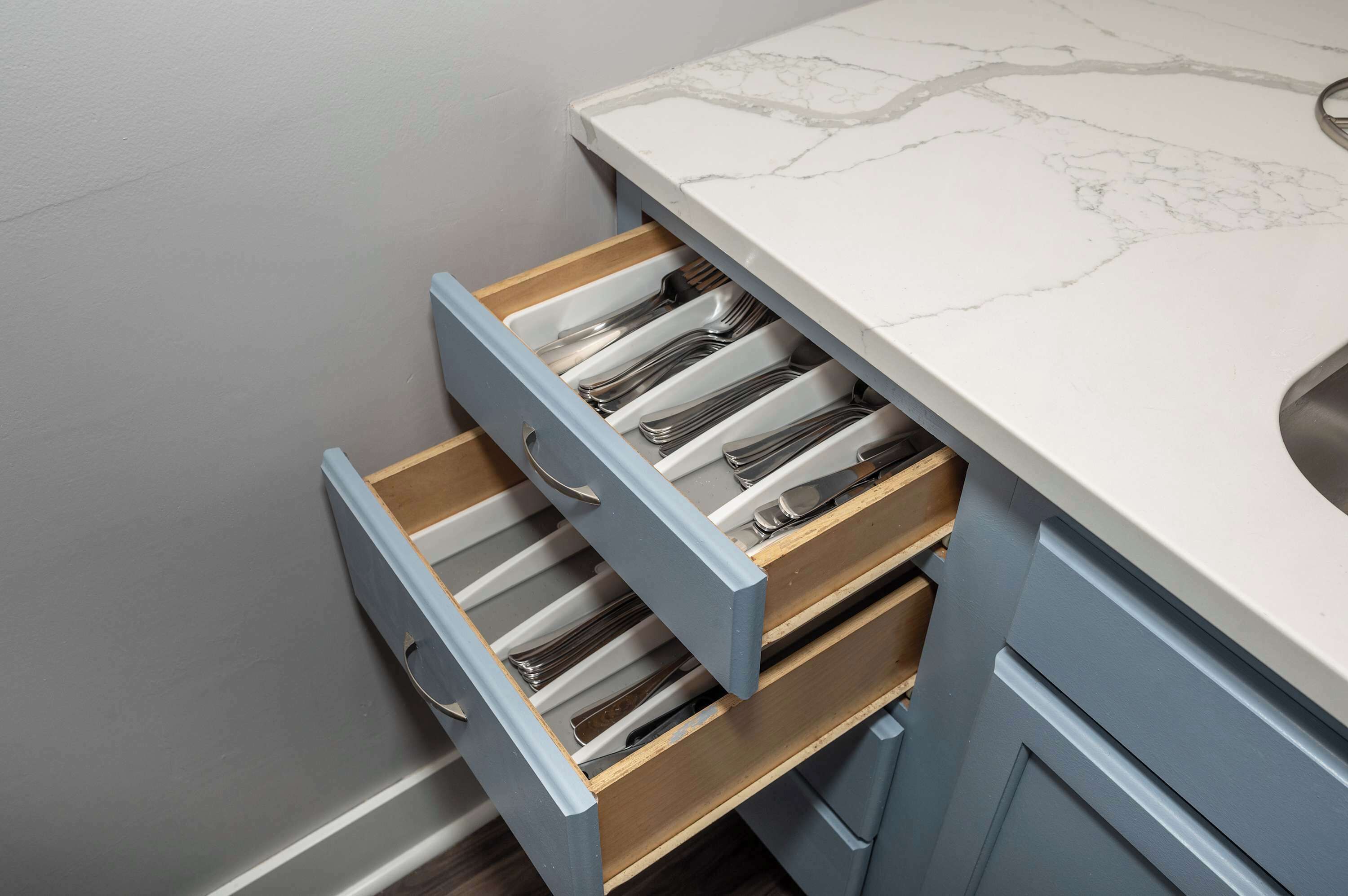 A kitchen with a marble countertop and a drawer with utensils.