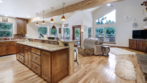 Una cocina amplia con armarios de madera y una isla grande, un espacio de sala acogedor con chimenea, y ventanas grandes que ofrecen vistas al exterior.