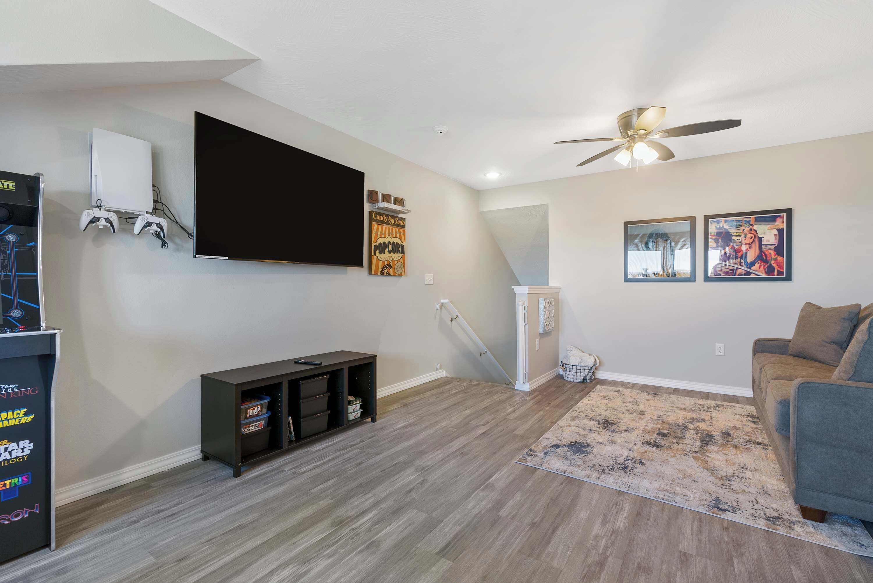 A living room with a flat-screen TV, gaming console, and a ceiling fan.