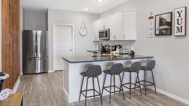 A modern kitchen with white cabinets, stainless steel appliances, and a bar area with stools. - A Little Slice of Branson - Ozarks Views (Branson)